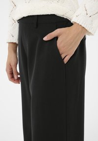 Fekete szabott nadrág sima textúrával, oldalsó zsebekkel és testhezálló derékkal, fehér kötött pulóverrel párosítva.