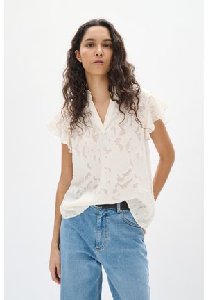 Blusa crema con maniche a volant, tessuto testurizzato con un sottile motivo, abbinata a jeans in denim blu a vita alta.