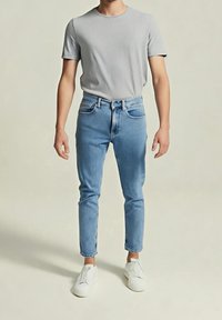 Šedé tričko s krátkým rukávem v kombinaci se světle modrými džínami. Džíny mají pět kapes a mírné opotřebení. Obuv tvoří bílé slip-on tenisky.