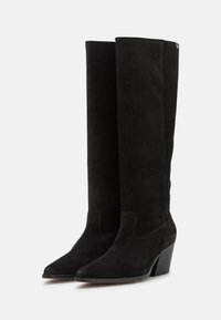 Bottes noires en suède, montantes jusqu'au genou, avec un bout pointu, une surface texturée et un talon épais. Présente un design sans coutures et des accents de couture subtils.