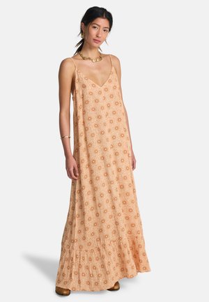 Abito lungo in tessuto arancione chiaro con motivo a stelle ripetute, scollo a v, spalline sottili e orlo arricciato. Indossato con scarpe marroni.