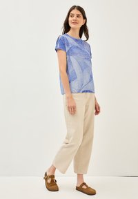 Top de manga corta azul con patrón, pantalones de pierna ancha beige y sandalias de ante marrón. Diseño simple con detalles sutiles en las mangas.