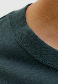 Tamnzelena pamučna majica, ovratnik, rebrasta tekstura, izbliza, s glatkom završnom obradom tkanine i vidljivim detaljima šivanja.