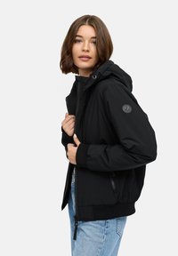 Črna kapuca z elastičnimi manšetami in zadrgo. Ima okroglo logotipno nalepko na rokavu ter gladko, sijajno teksturo.