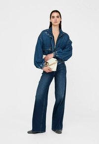 Denimist kärbitud jakk lõhkumisvarrukate, tõmbluku ja trukikinnitustega, kombineeritud laia säärega denimpükste ja ketiõlarihmaga kreemja käekotiga.