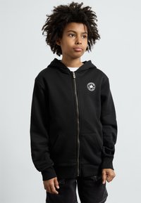 Felpa nera con zip realizzata in tessuto misto cotone, caratterizzata da una tasca a marsupio frontale e un'emblema rotondo sul lato sinistro del petto.