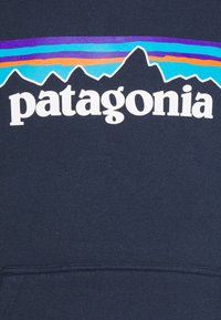 Sweatshirt azul marinho com um destacado logotipo branco "patagonia", sobreposto com gráficos coloridos de cadeias montanhosas em roxo, azul e laranja.