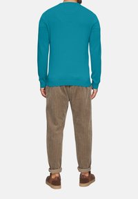 Tyrkysový sveter s okrúhlym výstrihom, príjemne rebrovanými manžetami a lemom, skombinovaný s béžovými kordové nohavicami a hnedými topánkami.