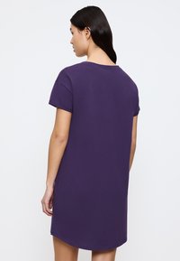 Fioletowa bawełniana sukienka t-shirtowa z krótkimi rękawami i okrągłym dekoltem, o luźnym kroju i lekko zaokrąglonym dołem z tyłu.