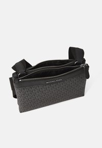 Black fabric bag with multiple zippered compartments, featuring a geometric pattern and a logo at the front. Adjustable strap included.