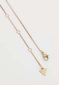 Gold metal chain necklace featuring a triangular pendant with "GUESS" engraved. Smooth surface with links and a lobster clasp closure.