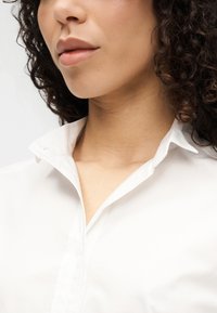 Λευκό πουκάμισο με γιακά, με λεία υφή, χαρακτηριστικό γιακά με εγκοπή, λεπτομέρεια με κουμπιά και στενή γραμμή, τοποθετημένο σε ουδέτερο φόντο.