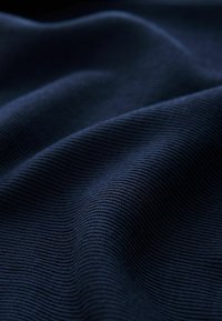 Stufă ribbed de culoare albastră închisă cu pliuri moi, creând un model texturat, ondulat sub o iluminare difuză.