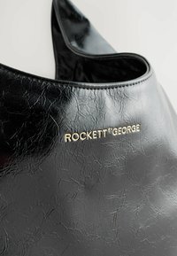 Fekete textúrájú műbőr táska laza formával. Elöl arany "ROCKETT ST GEORGE" márkázással. Simább, puha szélek.
