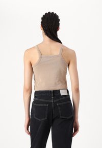 Béžový crop top na tenkých ramienkach, hladká textura a dizajn na chrbte. Skombinovaný s tmavými džínsami s vysokým pásom a jednoduchou nálepkou.