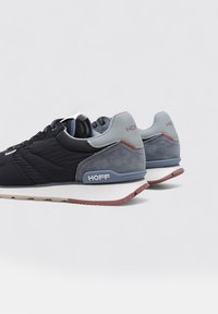 Zapatillas deportivas en negro y gris que combinan nylon y ante, con una entresuela blanca, acentos texturizados y detalles rojos en el talón.