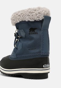 Bota Sorel à prova d'água em azul-marinho e preto. Apresenta um punho de pele cinza fofinho, ilhoses de metal e sola de borracha riscada branca para tração.
