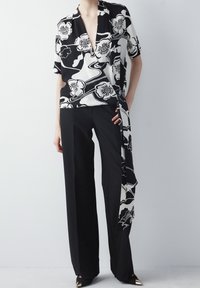 Blusa avvolgente a stampa floreale in bianco e nero con maniche corte, abbinata a pantaloni larghi neri, caratterizzati da una consistenza liscia e un design fluido.