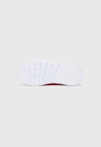Suela de goma blanca de una zapatilla con un patrón de dibujo en forma de cuadrícula y un logo visible de Nike en forma de swoosh cerca del talón.