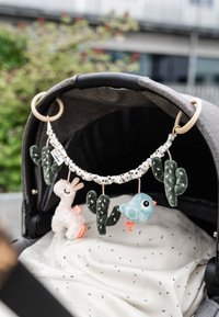 Zachte knuffelmobiel met ontwerpen van een lama, vogel en cactus in pasteltinten, bevestigd aan een grijze kinderwagen met een witte stoffen achtergrond.