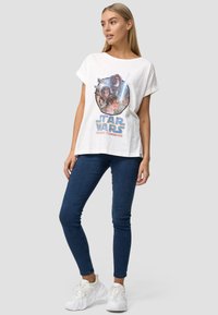 T-shirt bianco a maniche corte con una grafica colorata di "Star Wars" con i personaggi, abbinato a jeans skinny blu e sneakers bianche.