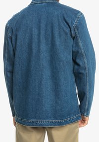 Kurtka dżinsowa w ciemnym niebieskim kolorze o prostym kroju, z długimi rękawami i kołnierzem z wydłużonymi końcami. Charakteryzuje się widocznymi przeszyciami i luźnym fasonem.