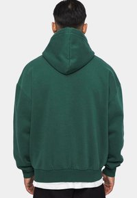 Groene hoodie met een grote capuchon, verlaagde schouders, geribbelde manchetten en zoom. Zacht materiaal met een gladde textuur. Achteraanzicht met minimale details.