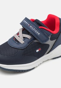 Scarpa sportiva blu navy con tomaia in mesh e sintetico, dettagli grigi e interno rosso. Presenta un cinturino in velcro e una suola testurizzata.
