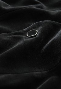 Black velvet fabric with a smooth texture, featuring a small, shiny hexagonal button positioned on a wrinkled surface.