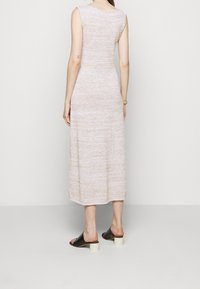 Abito senza maniche, lungo fino al ginocchio, in tessuto a maglia beige chiaro con una finitura testurizzata. Indossato con mule nere con tacco spesso di colore chiaro.