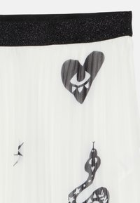 Mustat ja valkoiset laskostetut hameet, joissa on musta vyötärö, sydän-, silmä- ja käärmesuunnittelu sekä metalliset yksityiskohdat vyötärön ympäri.