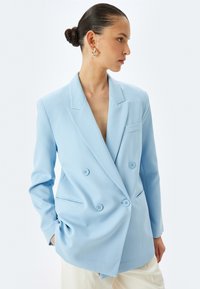 Lichtblauwe dubbelknopen blazer met notch-lapel, twee voorkeurszakken en knoopdetails; lijkt op maat gemaakt en is van een gladde stof.