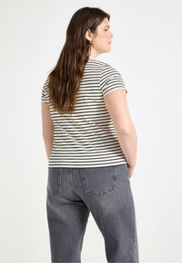 Stribet kortærmet t-shirt i creme og sort, ribbet tekstur, parret med højtaljede mørkegrå jeans med baglommer.