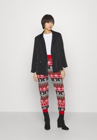 Blazer preto de dupla abotoadura sobre uma t-shirt branca, combinado com calças vermelhas e pretas com padrões e motivos de inverno, e botas pretas até ao tornozelo.
