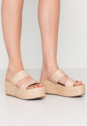 Beige Keilsandalen mit zwei geflochtenen Riemen, strukturiertem Obermaterial und korkähnlicher Plattform. Offene Zehenform mit einer leichten Wölbung in der Sohle.