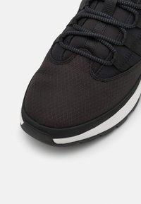 Černá sportovní bota s texturovaným svrškem s diamantovým vzorem, zesílenou špičkou a bílou mezipodešví. Šněrování je tmavé a tkané.
