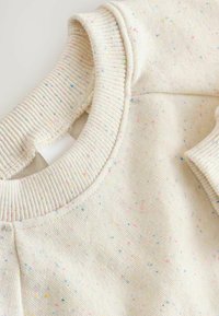 Kremowy sweatshirt z teksturowanym, prążkowanym dekoltem i kolorowymi plamkami w różowym, niebieskim i żółtym w całym materiale.