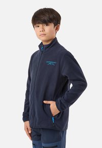 Tamsiai mėlyna vilnos striukė su aukštu apykakliu, užtrauktuku per visą ilgį, šoniniais kišenėmis ir mėlynu logotipu. Lygios tekstūros ir prigludusio dizaino, užtikrinantis patogumą.