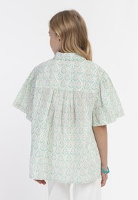 Kortärmad blus i ljusgrön blommönster, med krage och veckad bakdesign. Tillverkad av lättviktsmaterial.