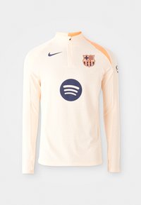 Light peach long-sleeve jersey with a high collar, featuring a blue Spotify logo and a Barcelona crest. Textured ribbed fabric detail.
