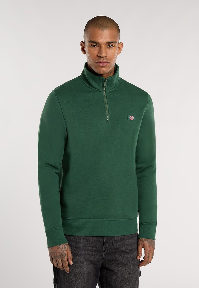 Groene sweatshirt met kwart-rits, gemaakt van dik materiaal, met een geribbelde kraag en boorden. Bevat een klein logo op de borst.