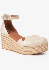 Chaussure à talon compensé avec une tige beige scintillante, semelle intérieure en cuir marron et semelle en corde tressée. Sangle de cheville ajustable incluse.