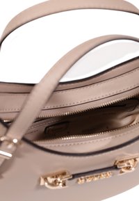 Bolso beige hecho de cuero sintético suave con hardware dorado, que cuenta con compartimentos de doble cremallera y un diseño estructurado.