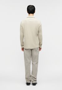 Μπεζ πόλο με μακριά μανίκια, μαλακό ύφασμα και άνετη εφαρμογή, συνδυασμένο με ανοιχτό γκρι παντελόνι με ίσια γραμμή, με υφή υφάσματος και διακριτικές ραφές.