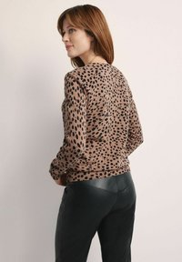 Sweter w panterkę w odcieniach beżu i czerni, okrągły dekolt, ściągacz na dolnej krawędzi, miękka struktura, w zestawieniu z czarnymi skórzanymi spodniami, widok z tyłu.