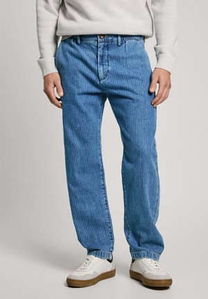 Ljusblå denimjeans med vertikala ränder, avslappnad passform, femficksdesign och knappstängning, ihop med vita sneakers.