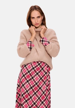 Beige knitted sweater with a high collar, paired with a pink and black patterned skirt featuring houndstooth design and flowing texture.