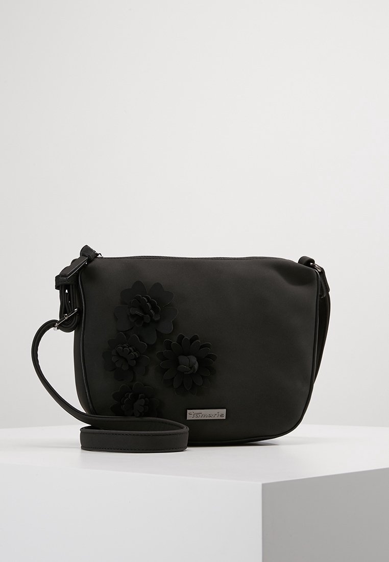 Schwarze synthetische Umhängetasche mit floralen Akzenten, flaches Design, verstellbarer Tragegurt und silberne Hardware-Logodetails. Glatte Oberfläche.