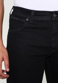 Black denim jeans featuring a close-fitting design, five-pocket style, subtle stitching, and a button closure on the waistband.