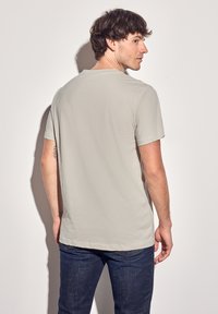 Vaaleanharmaa lyhythihainen t-paita, pehmeä kangas, rento malli, pyöreä pääntie, näkyvät saumat, yhdistetty tummansinisiin farkkuihin, yksinkertainen muotoilu.